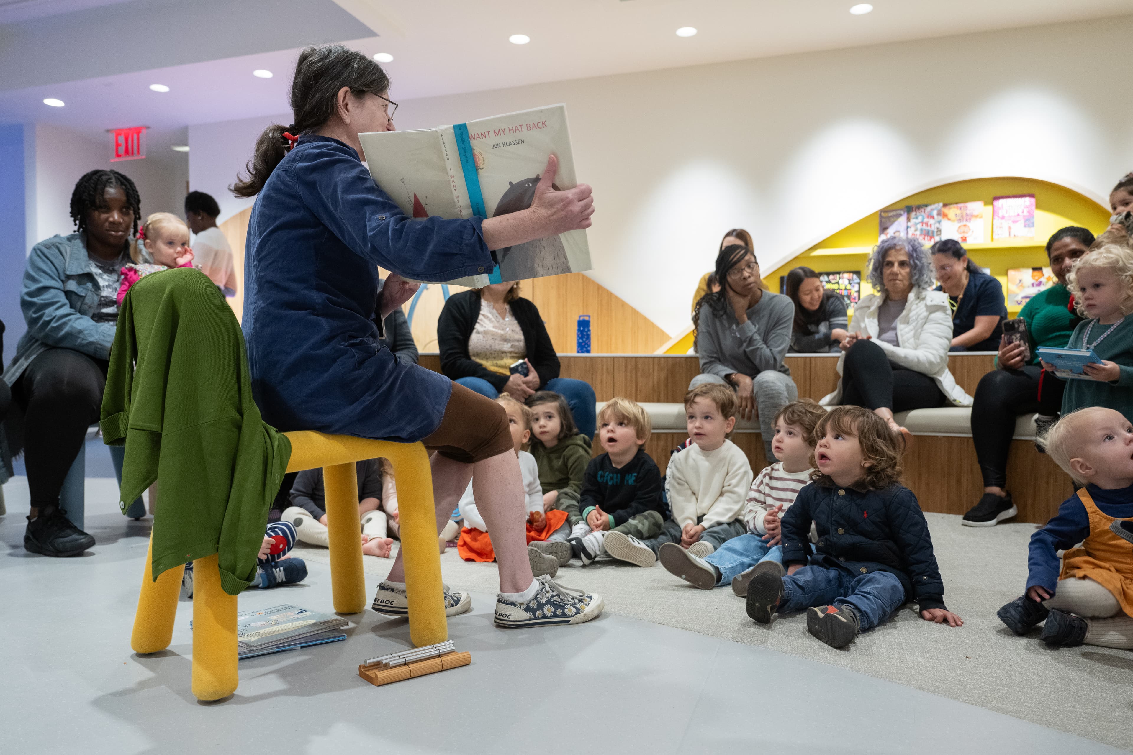 Toddlers are sat on the floor, gathered around a storyteller showing them a picture book.